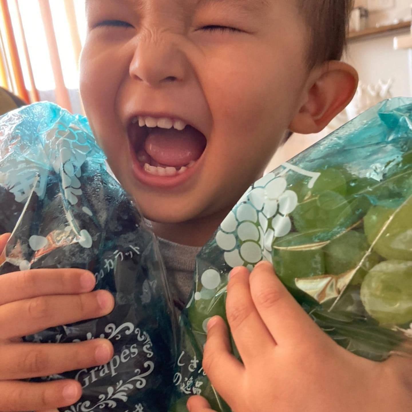 お子様がぶどうを両手に持ち、笑顔の画像